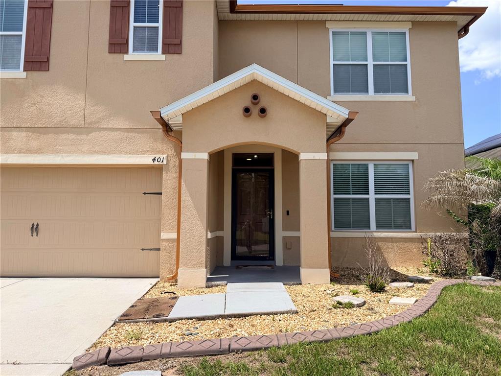 A two-story tan stucco house features a covered entryway, a garage, and brown shutters — 401 BRIAR PATCH LOOP, DAVENPORT, FL