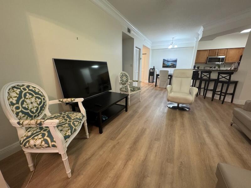 A living room features light wood-look flooring, a television on a stand, and several chairs — 9873 Baywinds Boulevard # 5203, West Palm Beach FL 33411, WEST PALM BEACH, FL