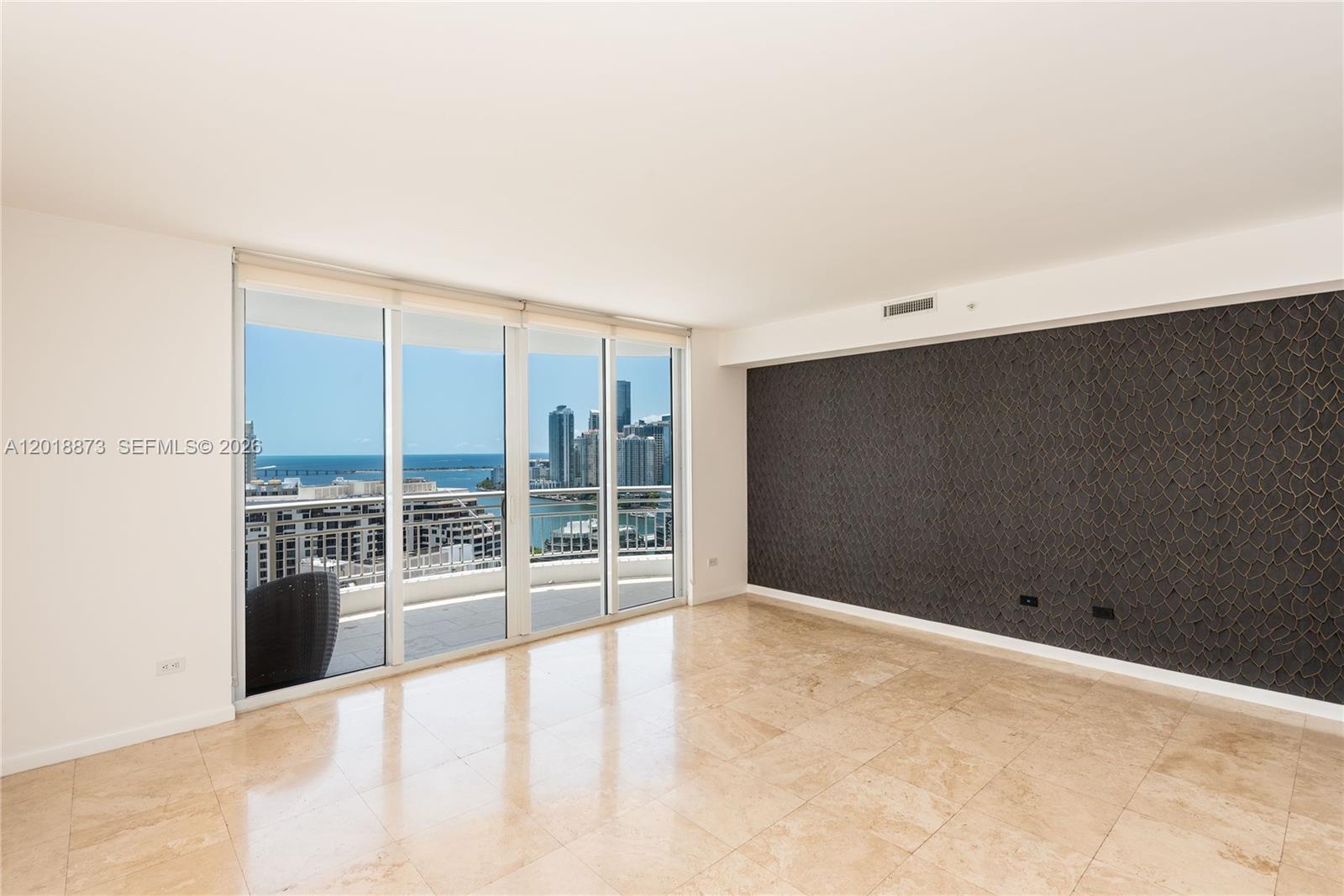 An empty room features beige tile flooring, a dark textured accent wall, and floor-to-ceiling windows — 848 Brickell Key Dr # 2703, Miami FL 33131, MIAMI, FL