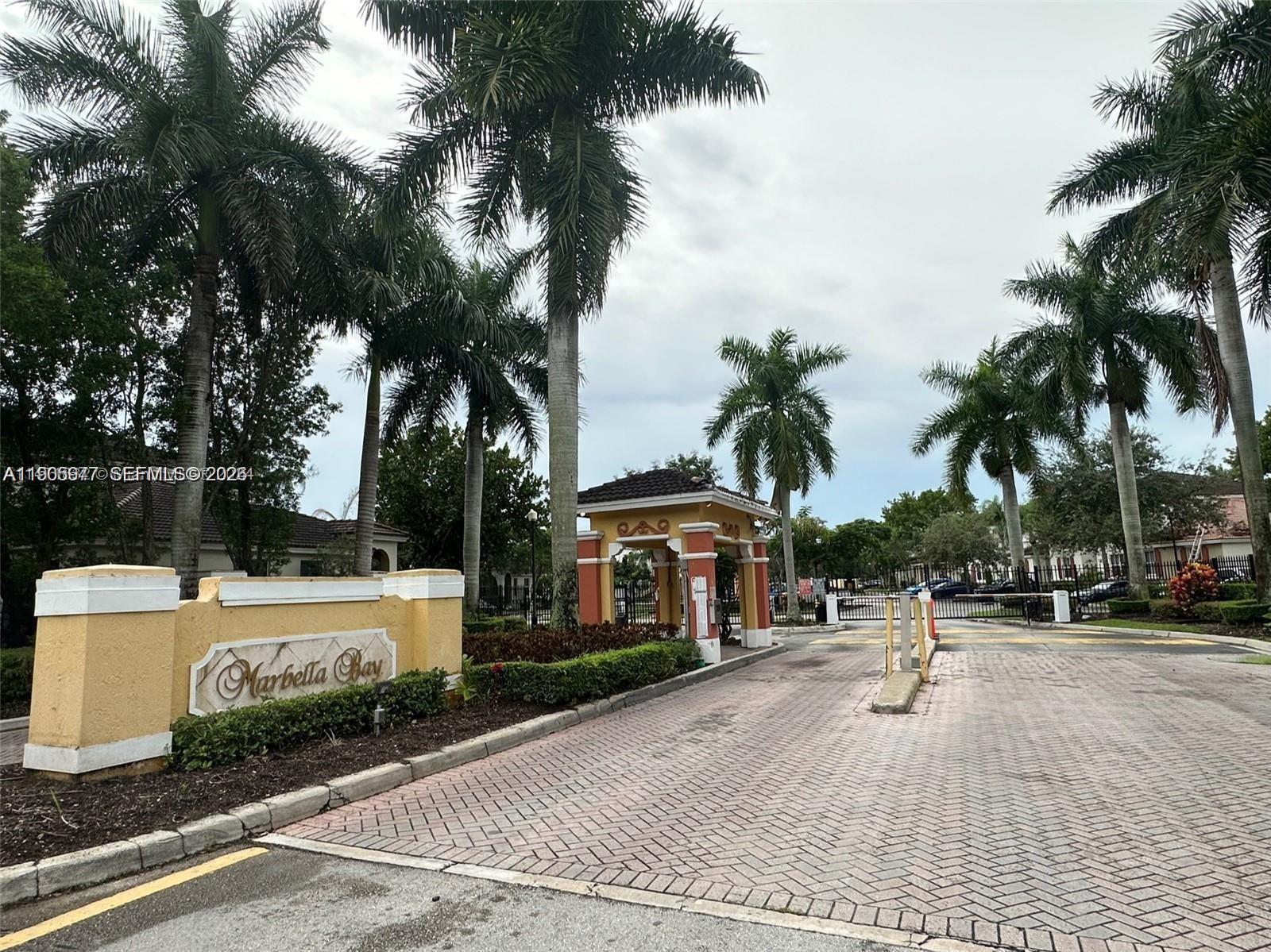 The gated entrance to the Marbella Bay community features a brick driveway and palm trees — 1040 NE 42nd Pl, Homestead FL 33033, HOMESTEAD, FL
