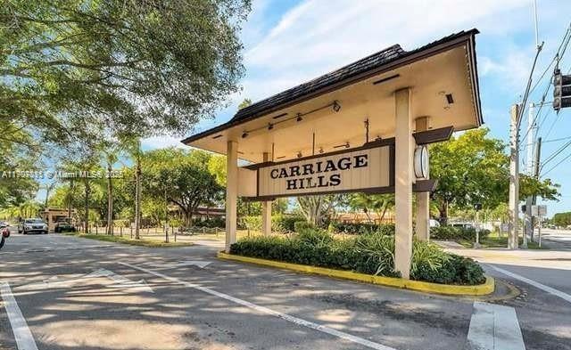 A large wooden entrance sign for Carriage Hills stands over a paved road with trees — 200 Berkley Rd # 113, Hollywood FL 33024, HOLLYWOOD, FL