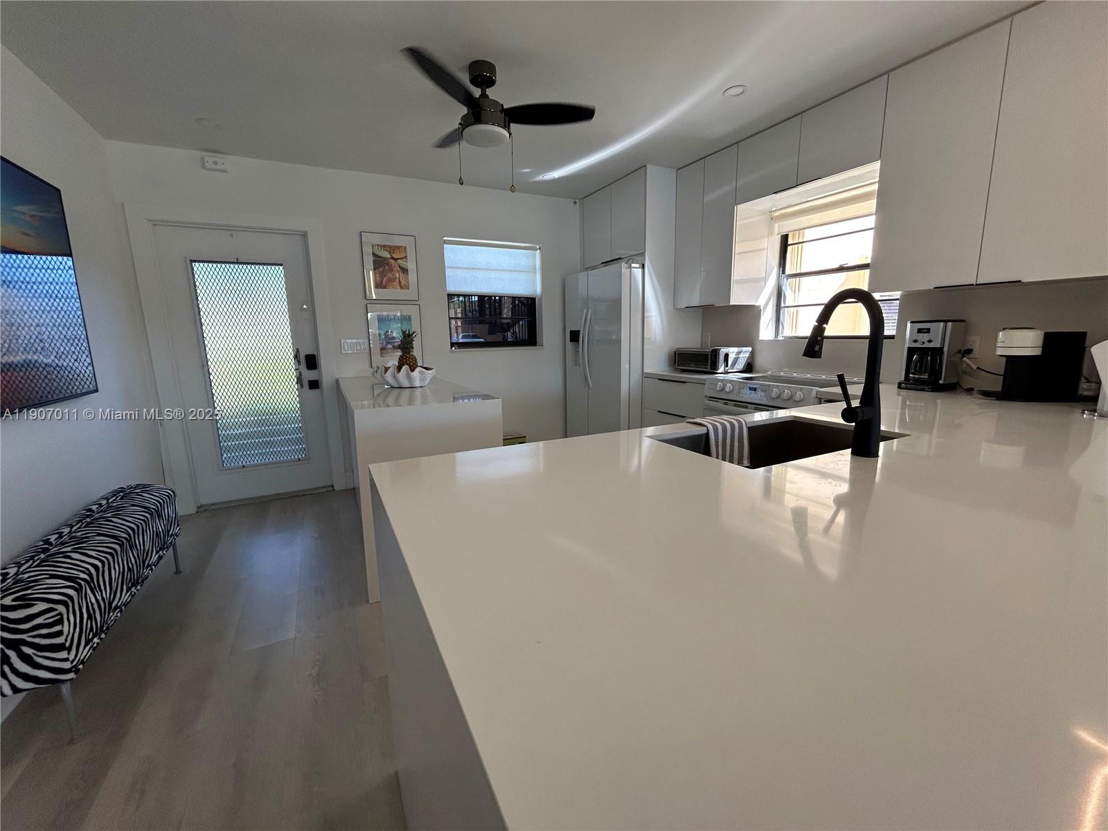 A modern kitchen features white cabinetry, quartz countertops, a black faucet, and a ceiling fan — 200 Berkley Rd # 113, Hollywood FL 33024, HOLLYWOOD, FL