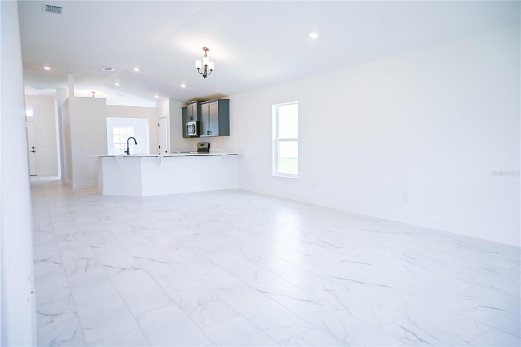 An open-concept living area features white marble-look tile flooring and a kitchen with dark cabinets — 3135 NE 45TH AVENUE, OCALA, FL
