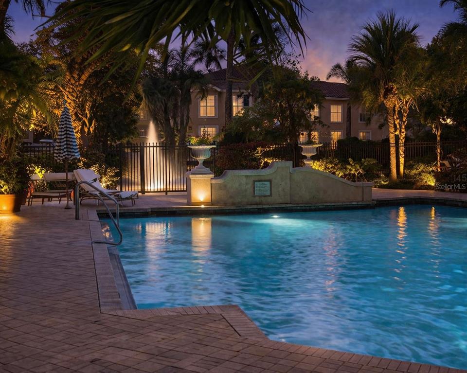 A swimming pool with a fountain and lounge chairs at dusk in front of a building — 4126 CENTRAL SARASOTA PARKWAY UNIT 2011, SARASOTA, FL