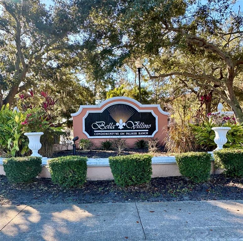 A sign for Bella Villino Condominiums on Palmer Ranch stands amidst trees and landscaping — 4126 CENTRAL SARASOTA PARKWAY UNIT 2011, SARASOTA, FL