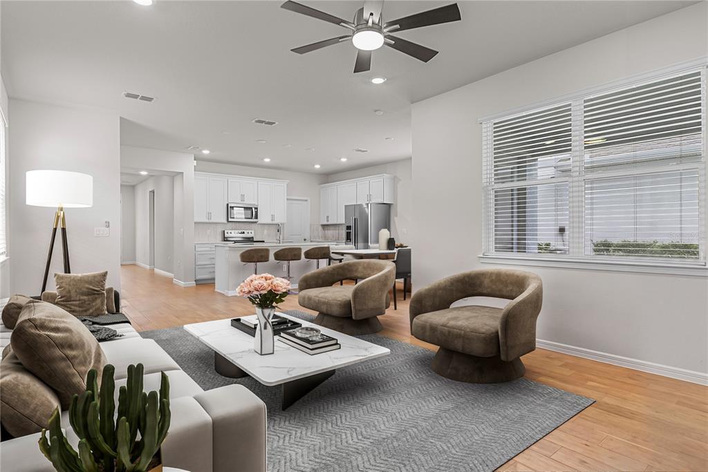 An open-concept living room and kitchen featuring white cabinetry, wood flooring, and modern furniture — 14250 LANIKAI BEACH DRIVE, ORLANDO, FL