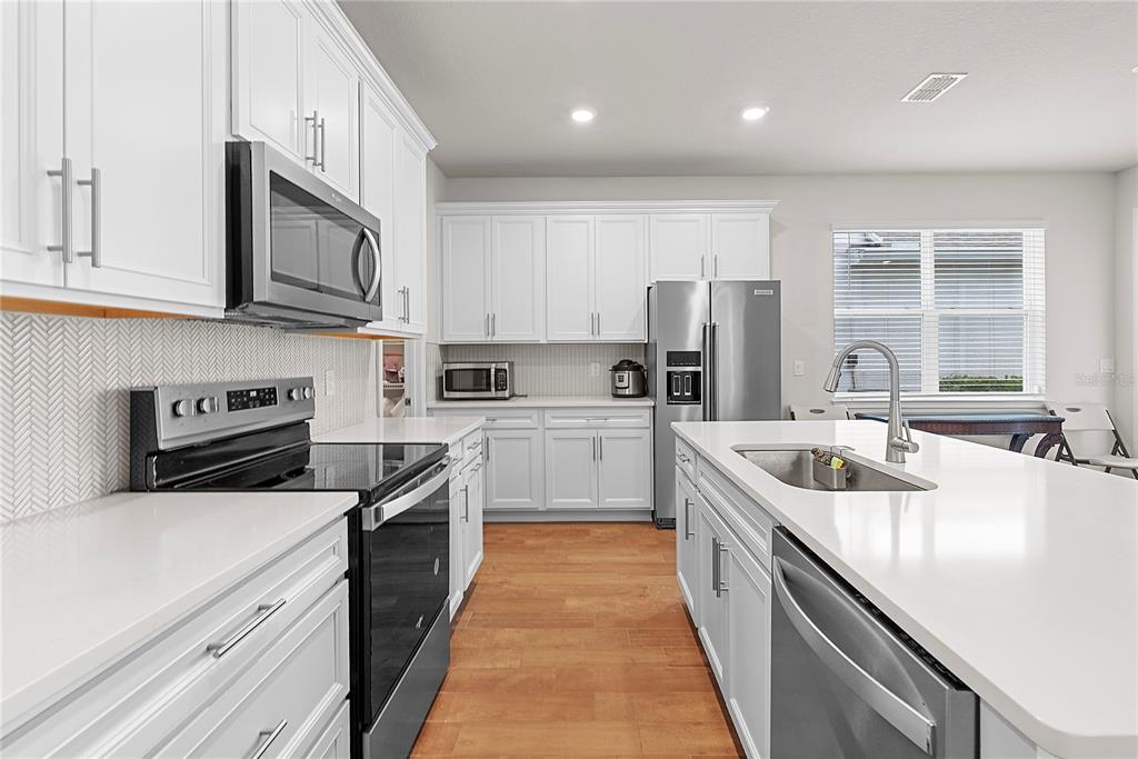 A modern kitchen features white cabinets, stainless steel appliances, quartz countertops, and wood-look flooring — 14250 LANIKAI BEACH DRIVE, ORLANDO, FL