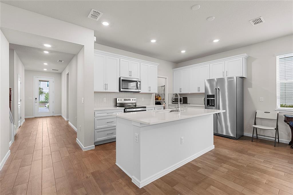 A white kitchen features a central island, stainless steel appliances, and light wood-look flooring — 14250 LANIKAI BEACH DRIVE, ORLANDO, FL