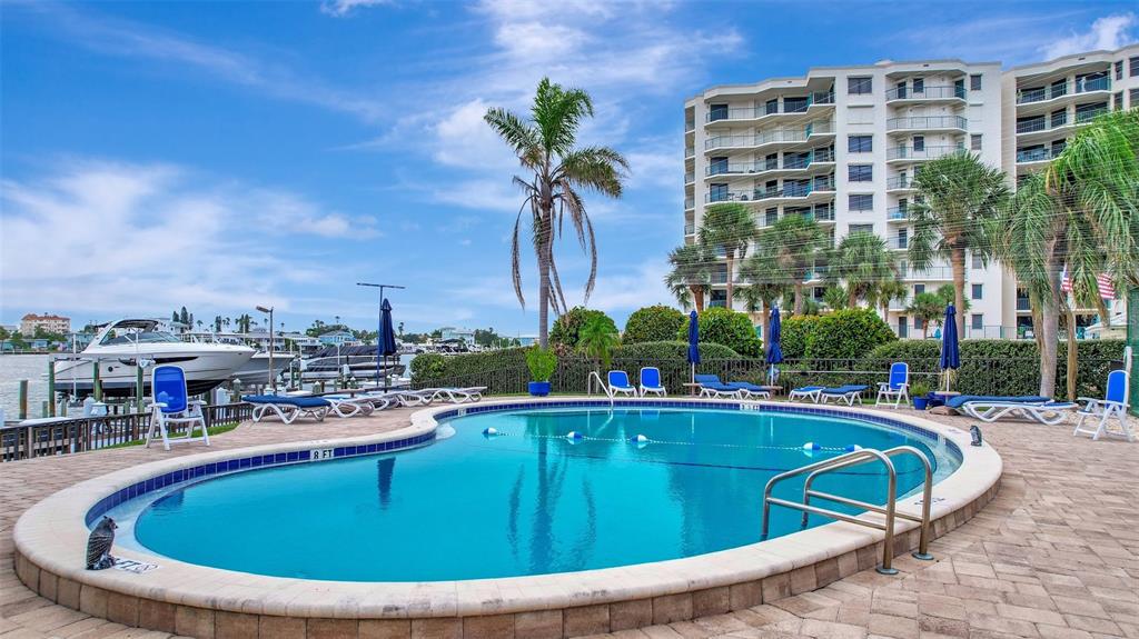 A swimming pool with lounge chairs sits on a patio next to a multi-story building — 660 ISLAND WAY UNIT 708, CLEARWATER BEACH, FL