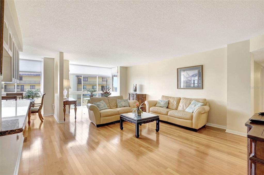 A living room with hardwood floors, two beige sofas, and large windows overlooking a building — 660 ISLAND WAY UNIT 708, CLEARWATER BEACH, FL