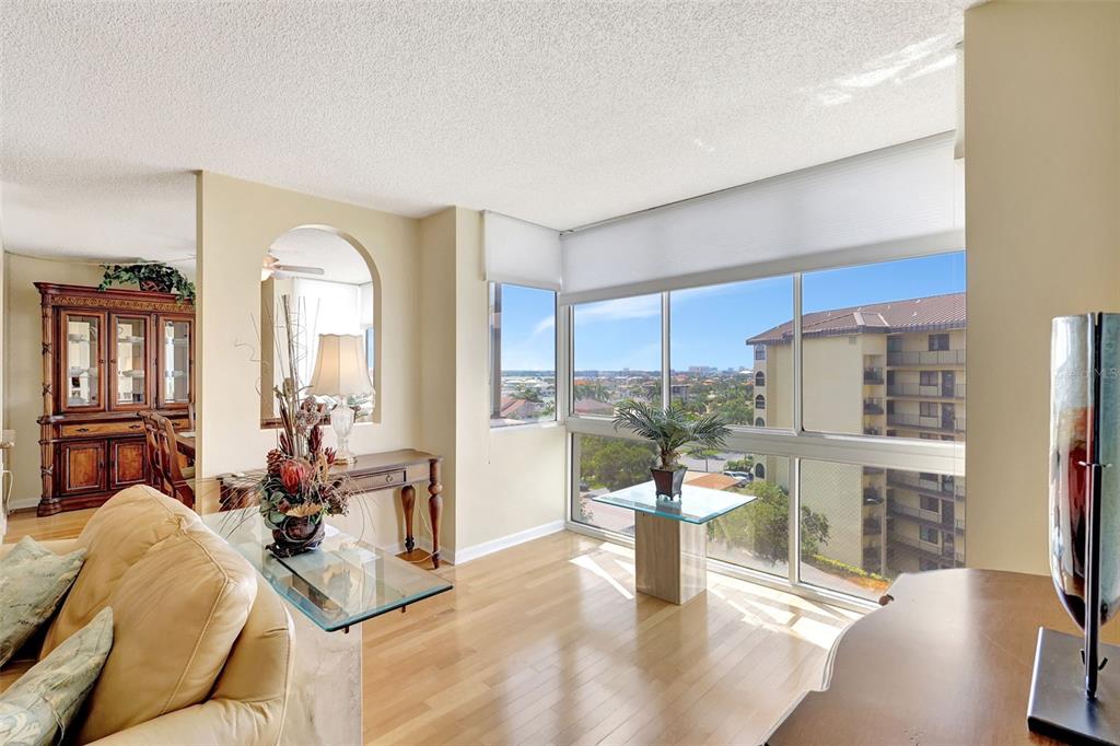A living room with hardwood floors, a glass-topped table, and large windows overlooking a building — 660 ISLAND WAY UNIT 708, CLEARWATER BEACH, FL