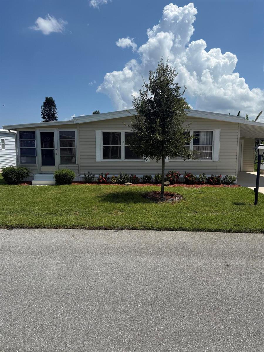 A single-story beige manufactured home features a front porch, a central tree, and landscaping — 463 Onyx Way, Jensen Beach FL 34957, JENSEN BEACH, FL