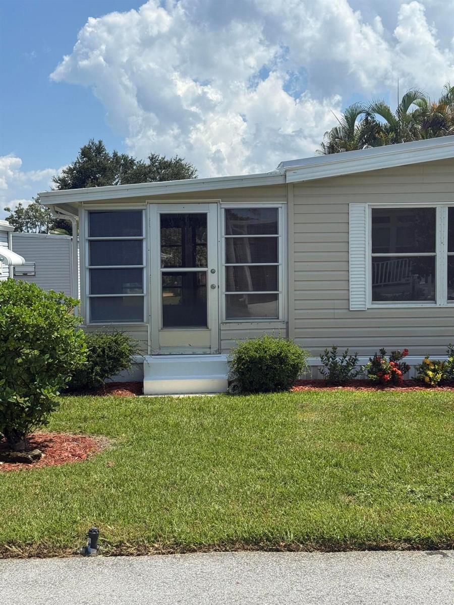 The exterior of a tan mobile home features a screened-in porch with a central door — 463 Onyx Way, Jensen Beach FL 34957, JENSEN BEACH, FL