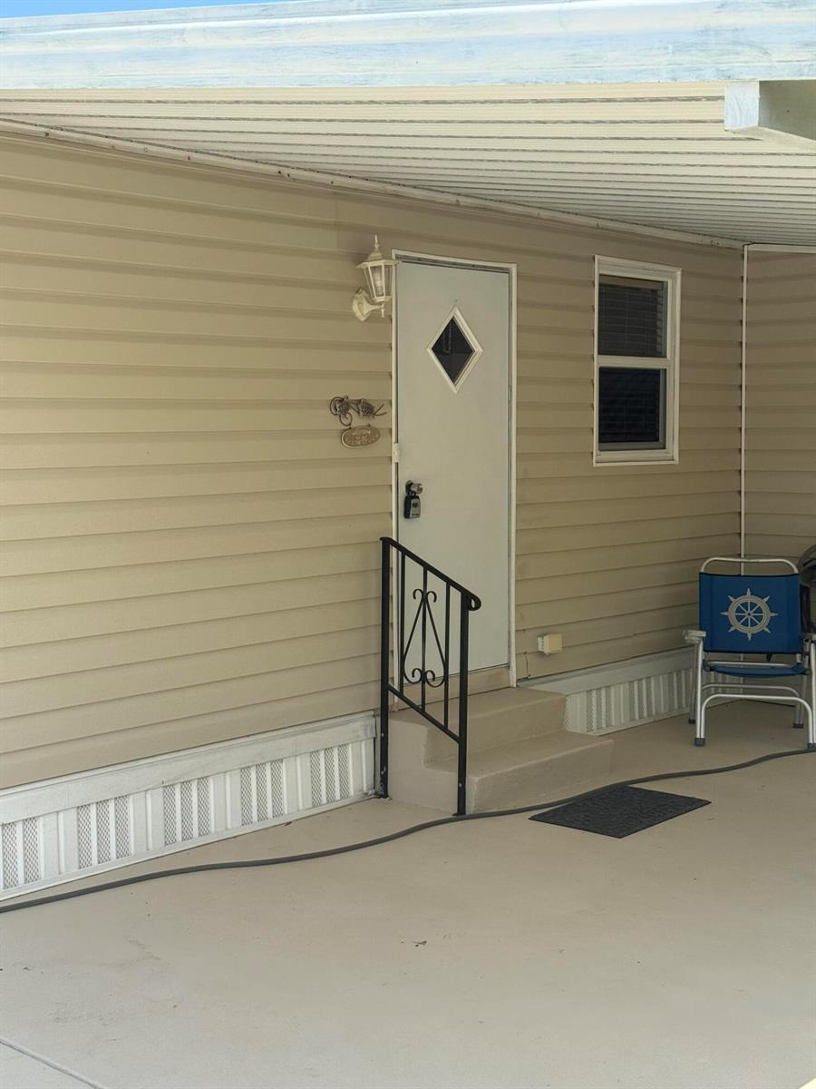 A beige mobile home exterior features a white door, a small staircase, and a carport — 463 Onyx Way, Jensen Beach FL 34957, JENSEN BEACH, FL