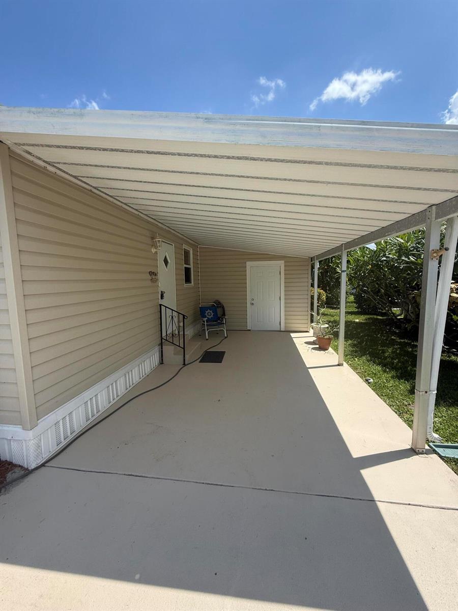 A beige mobile home features a covered concrete carport and two white exterior doors — 463 Onyx Way, Jensen Beach FL 34957, JENSEN BEACH, FL