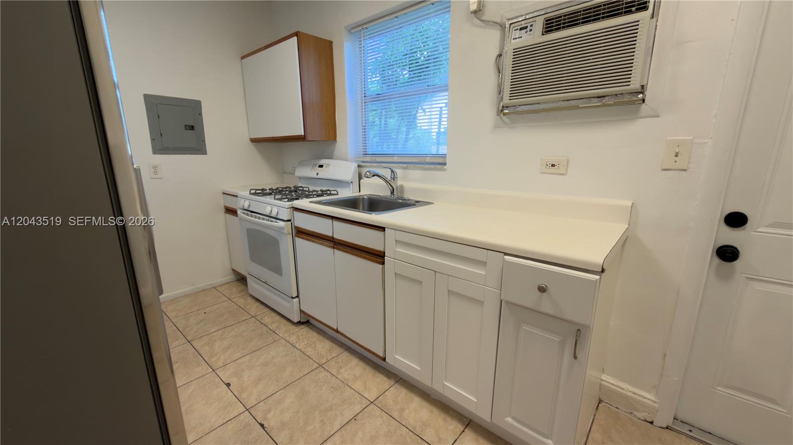 A small kitchen features white cabinets, a gas stove, a sink, and a window unit — 808 84th St # 810, Miami Beach FL 33141, MIAMI BEACH, FL