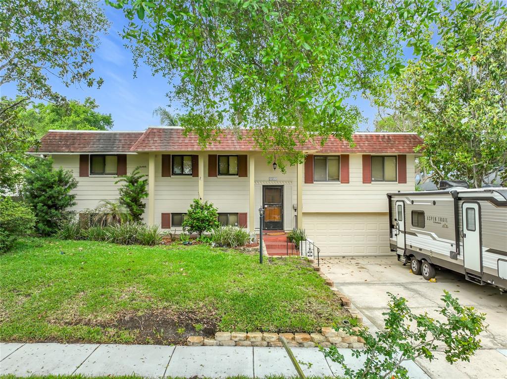 A split-level house with beige siding, a red shingled roof, and a parked travel trailer — 1511 GLASTONBERRY ROAD, MAITLAND, FL