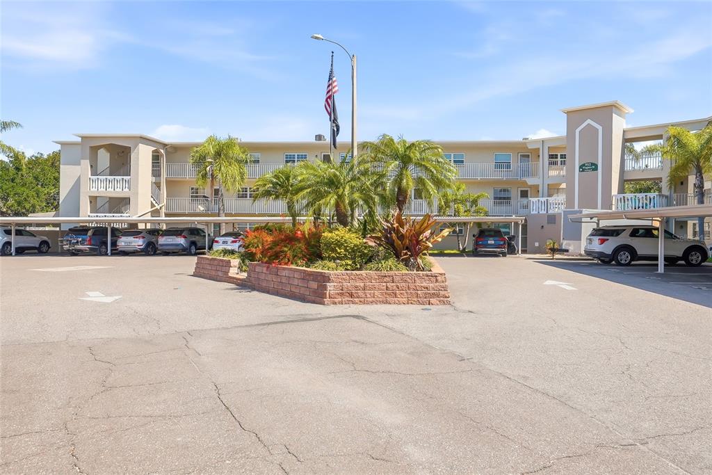 A three-story apartment building with a covered parking area and several parked cars — 952 VIRGINIA STREET UNIT 202, DUNEDIN, FL
