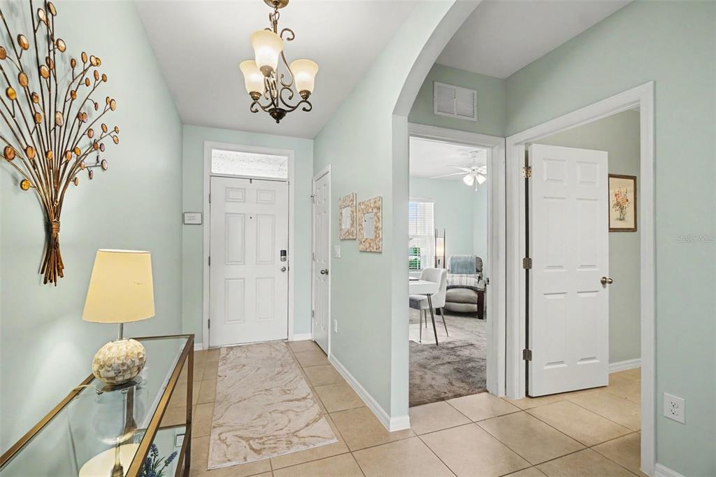A bright entryway features light blue walls, tile flooring, a chandelier, and a glass console table — 7048 WATERFORD PARKWAY, PUNTA GORDA, FL
