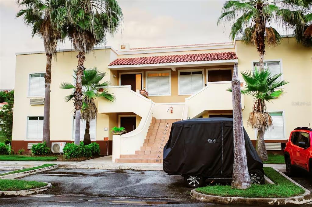A two-story yellow stucco building features an exterior staircase, palm trees, and a covered cart — 180 PALMAS DRIVE UNIT 27C, HUMACAO, PR