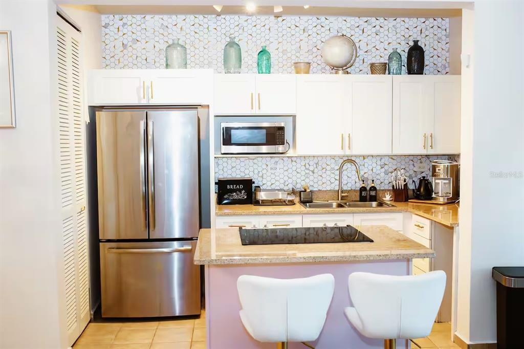 A kitchen features white cabinets, stainless steel appliances, a granite island, and a hexagonal backsplash — 180 PALMAS DRIVE UNIT 27C, HUMACAO, PR