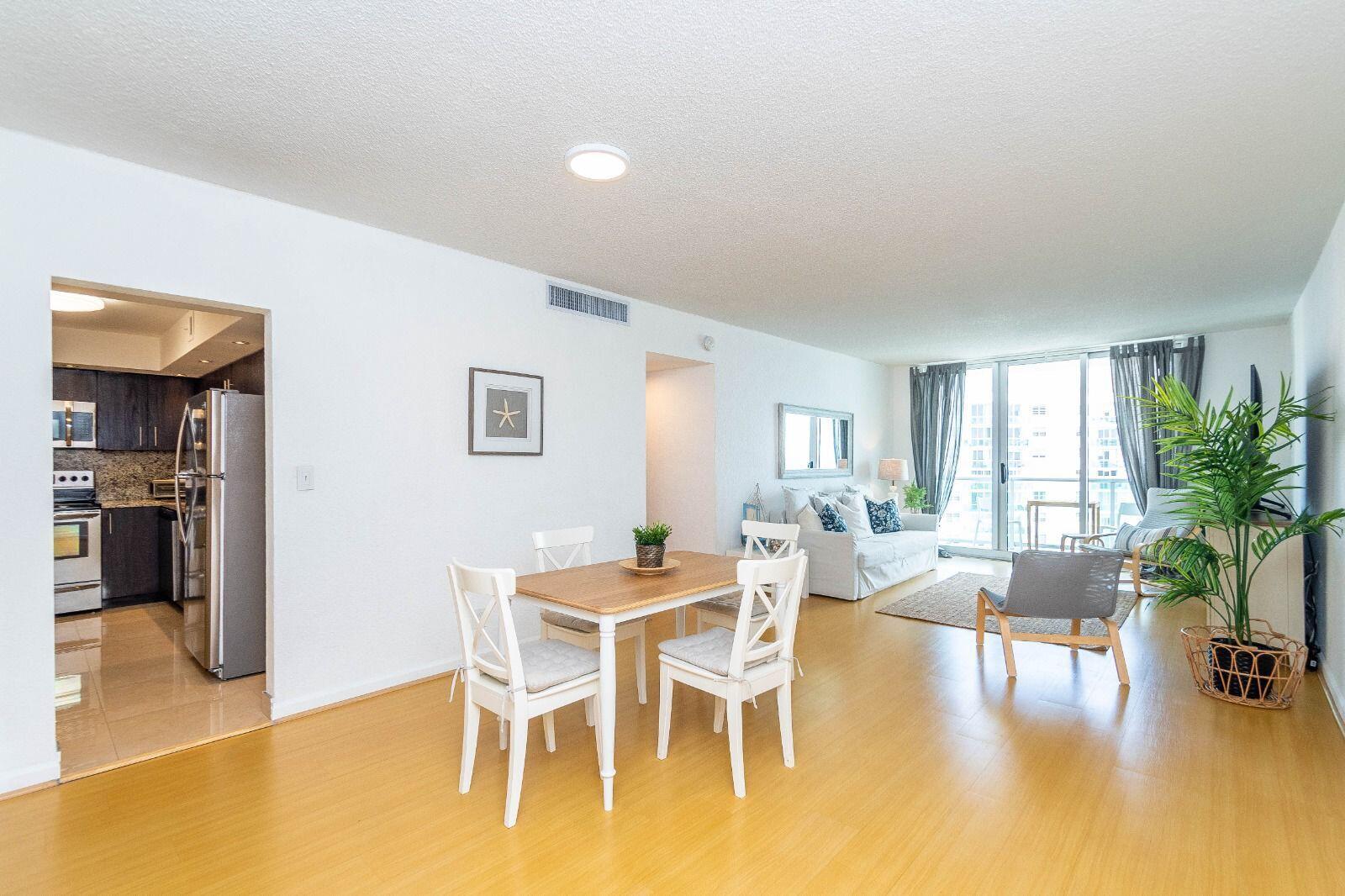 A bright living and dining area with light wood floors, white furniture, and a kitchen — 3901 S Ocean Drive # 14c, Hollywood FL 33019, HOLLYWOOD, FL