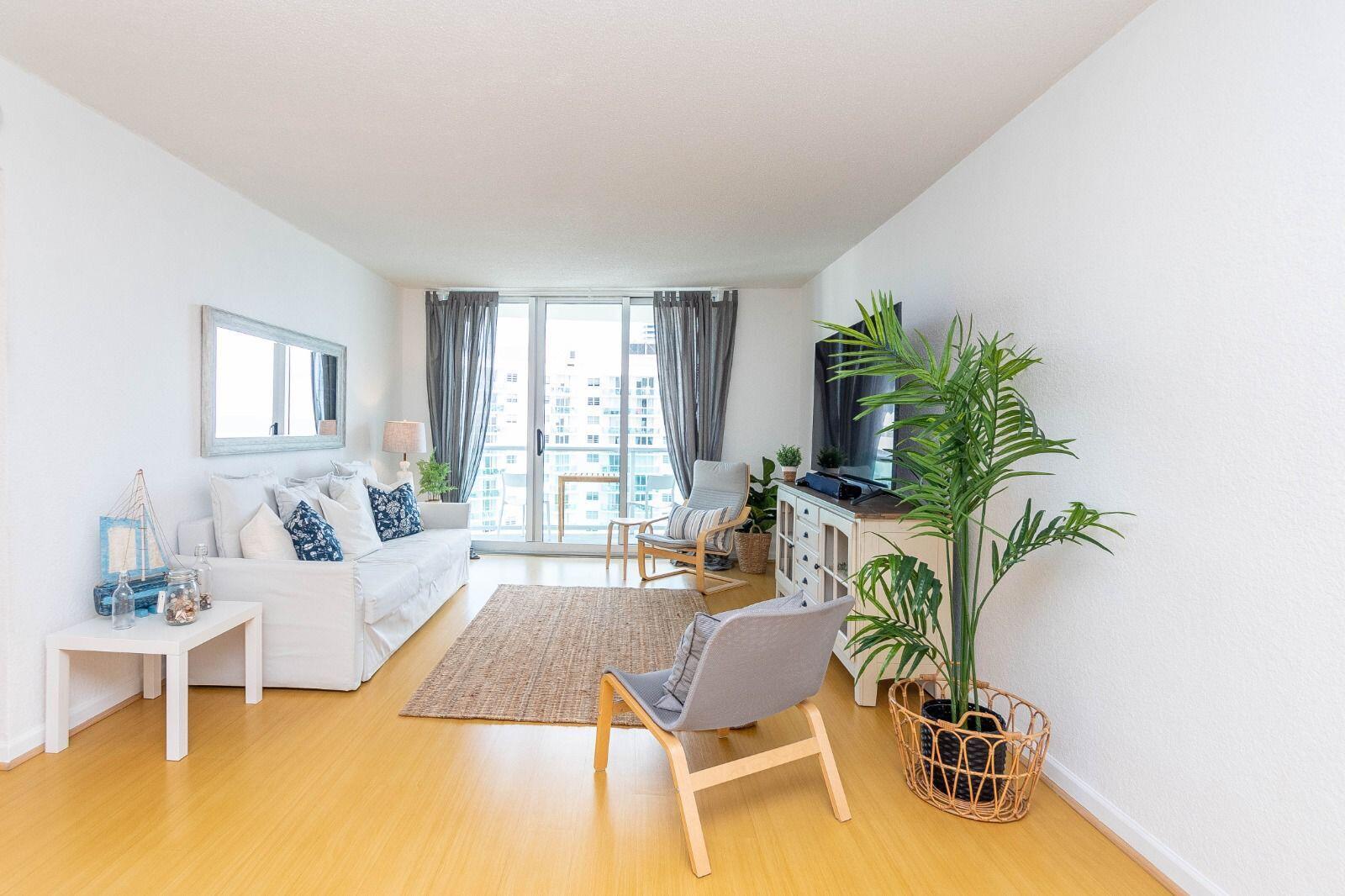 A bright living room features a white sofa, two armchairs, a television, and a large plant — 3901 S Ocean Drive # 14c, Hollywood FL 33019, HOLLYWOOD, FL
