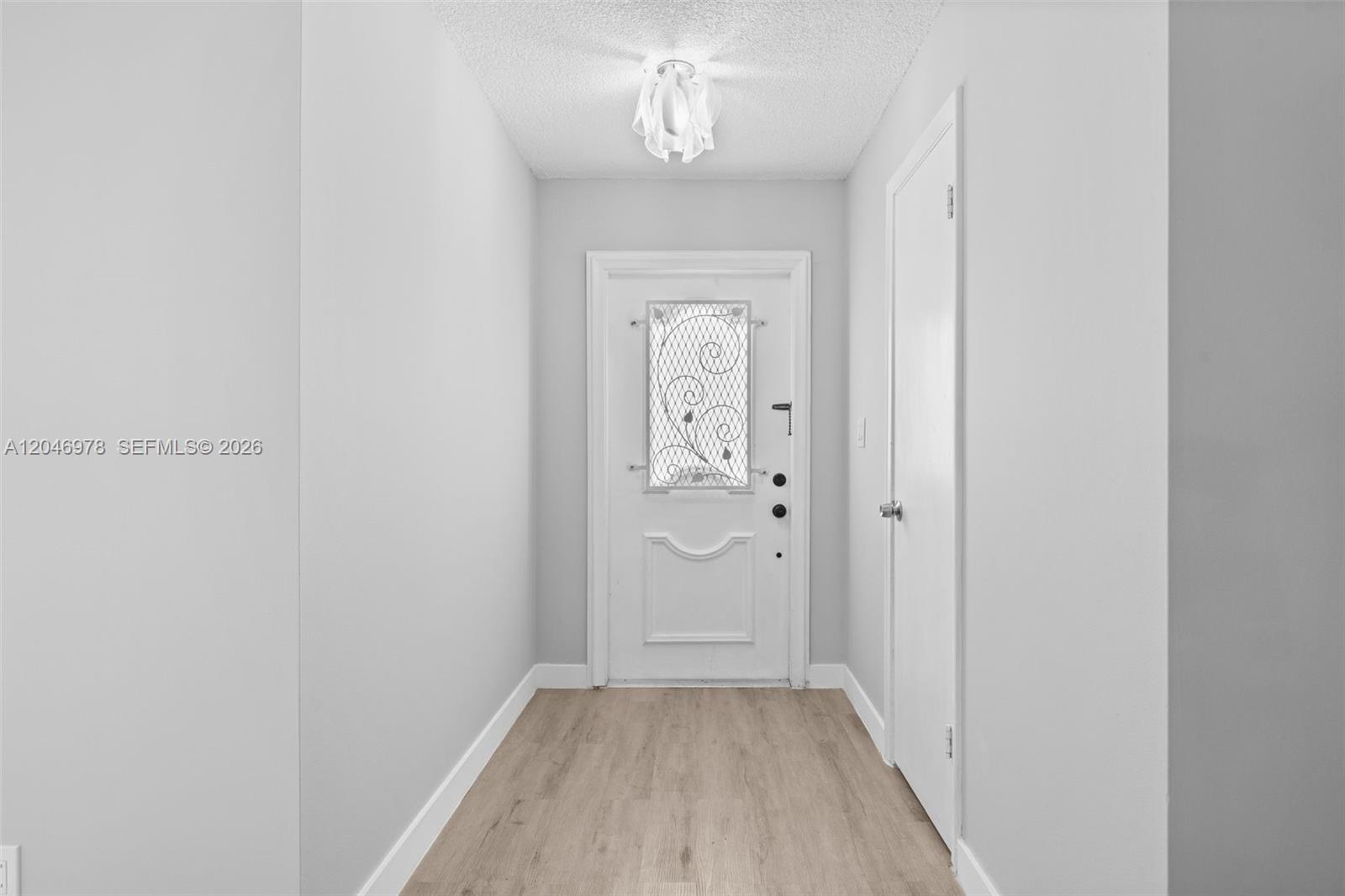 A white front door with a decorative glass insert sits at the end of a hallway — 2408 NE 10th St # 122, Hallandale Beach FL 33009, HALLANDALE BEACH, FL