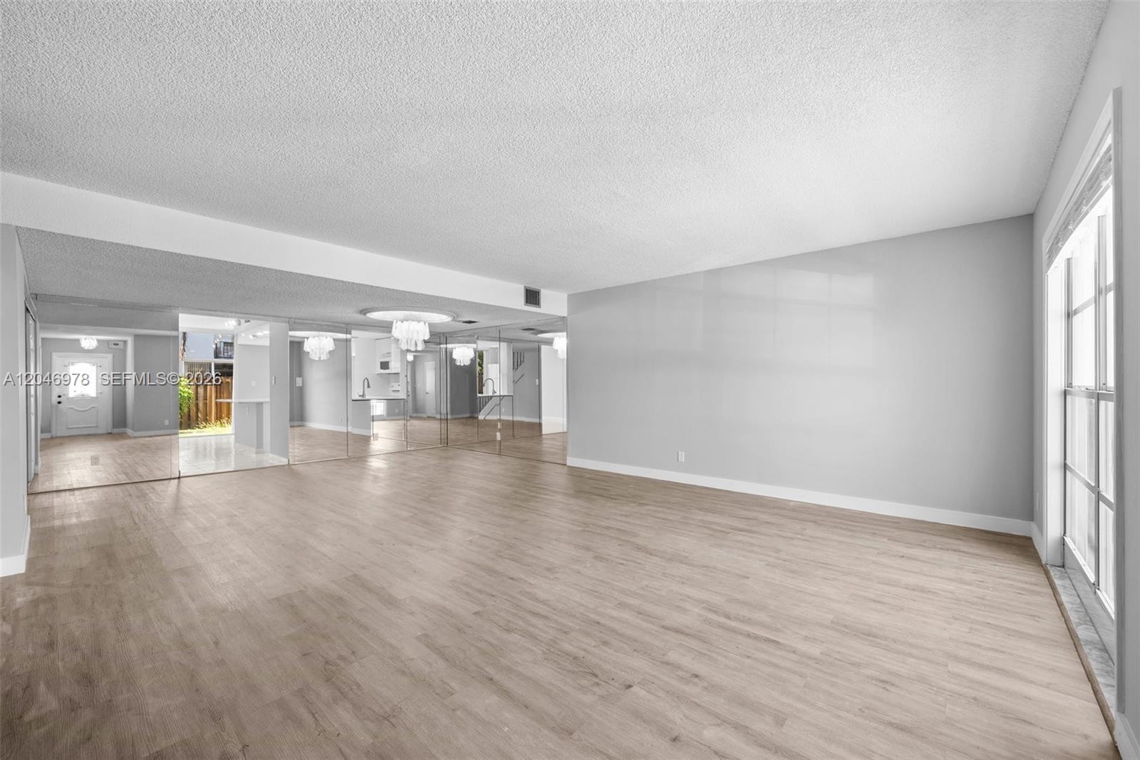 An empty living room features light wood-look flooring, gray walls, and a mirrored accent wall — 2408 NE 10th St # 122, Hallandale Beach FL 33009, HALLANDALE BEACH, FL