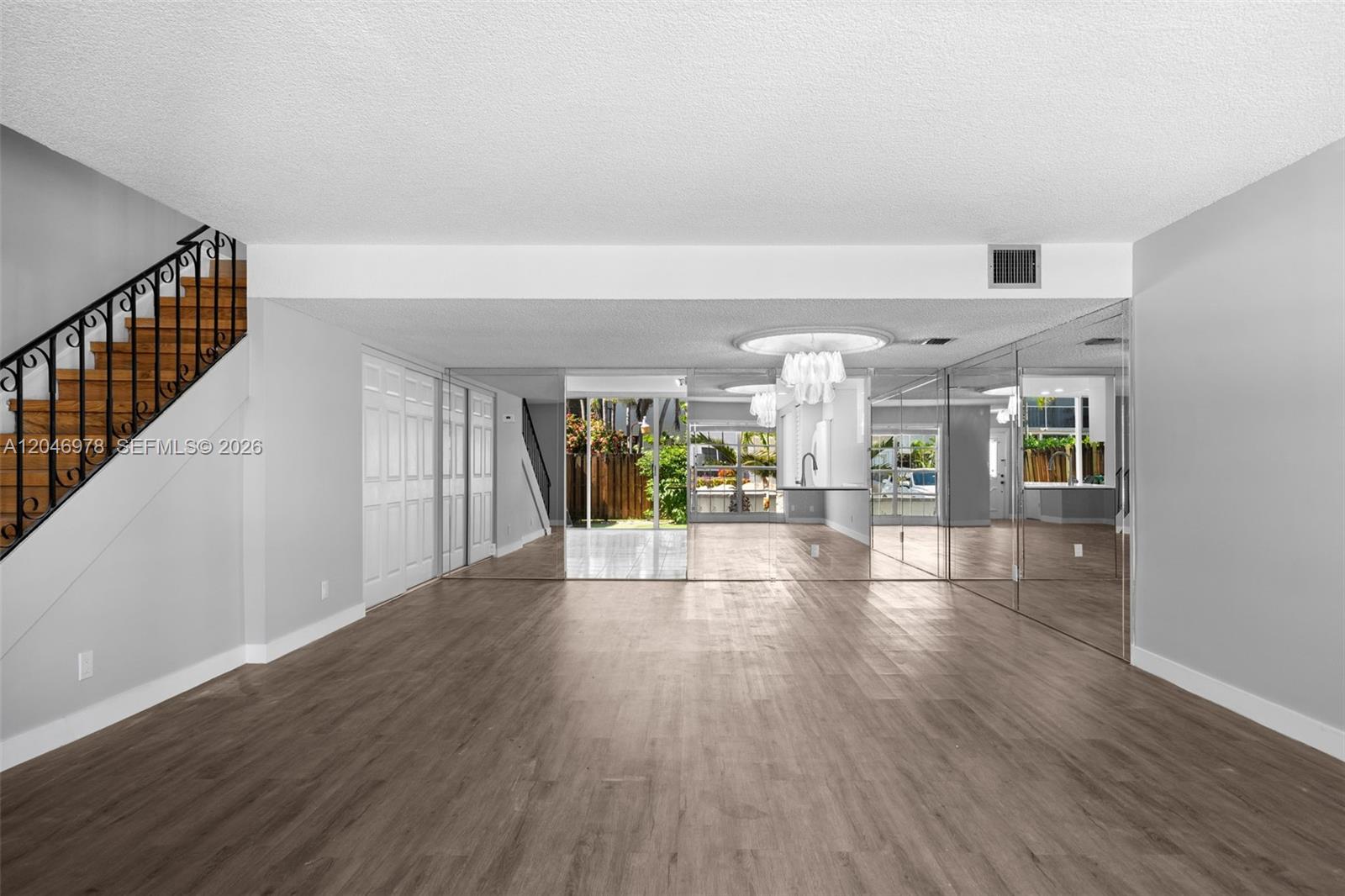 An empty room features wood-look flooring, a staircase with a black railing, and mirrored walls — 2408 NE 10th St # 122, Hallandale Beach FL 33009, HALLANDALE BEACH, FL
