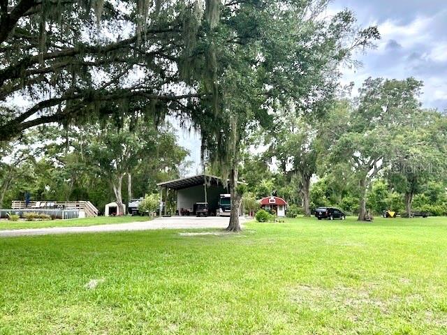 A large grassy yard features a metal carport, a small shed, and mature oak trees — 528 ASHLEY LANE, CENTER HILL, FL