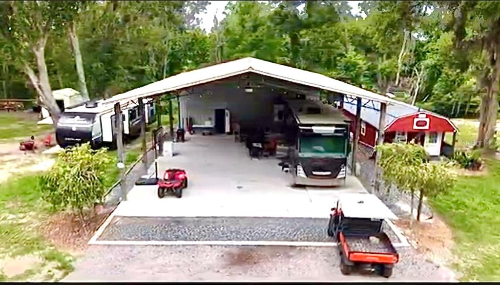 An aerial view shows a large metal carport sheltering a motorhome and a small red shed — 528 ASHLEY LANE, CENTER HILL, FL