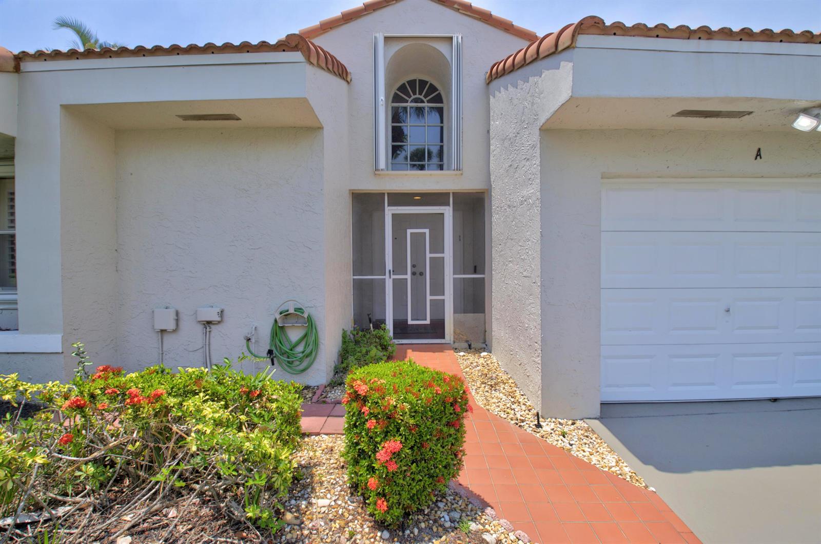 The exterior of a stucco home features a tiled roof, a garage, and a walkway — 10911 Ladera Lane # A, Boca Raton FL 33498, BOCA RATON, FL