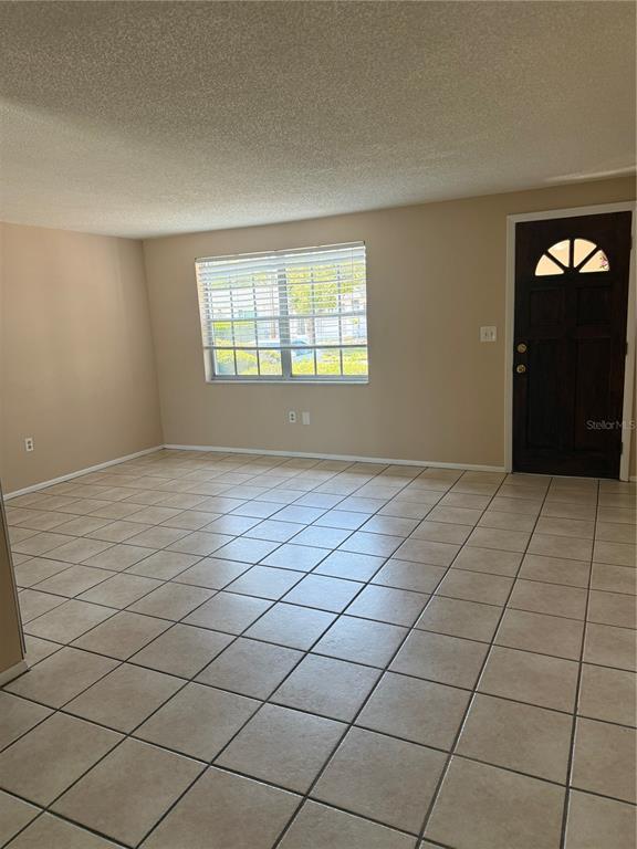 An empty room with beige walls, tile flooring, a window with blinds, and a front door — 4244 SHELDON PLACE UNIT 4244, NEW PORT RICHEY, FL