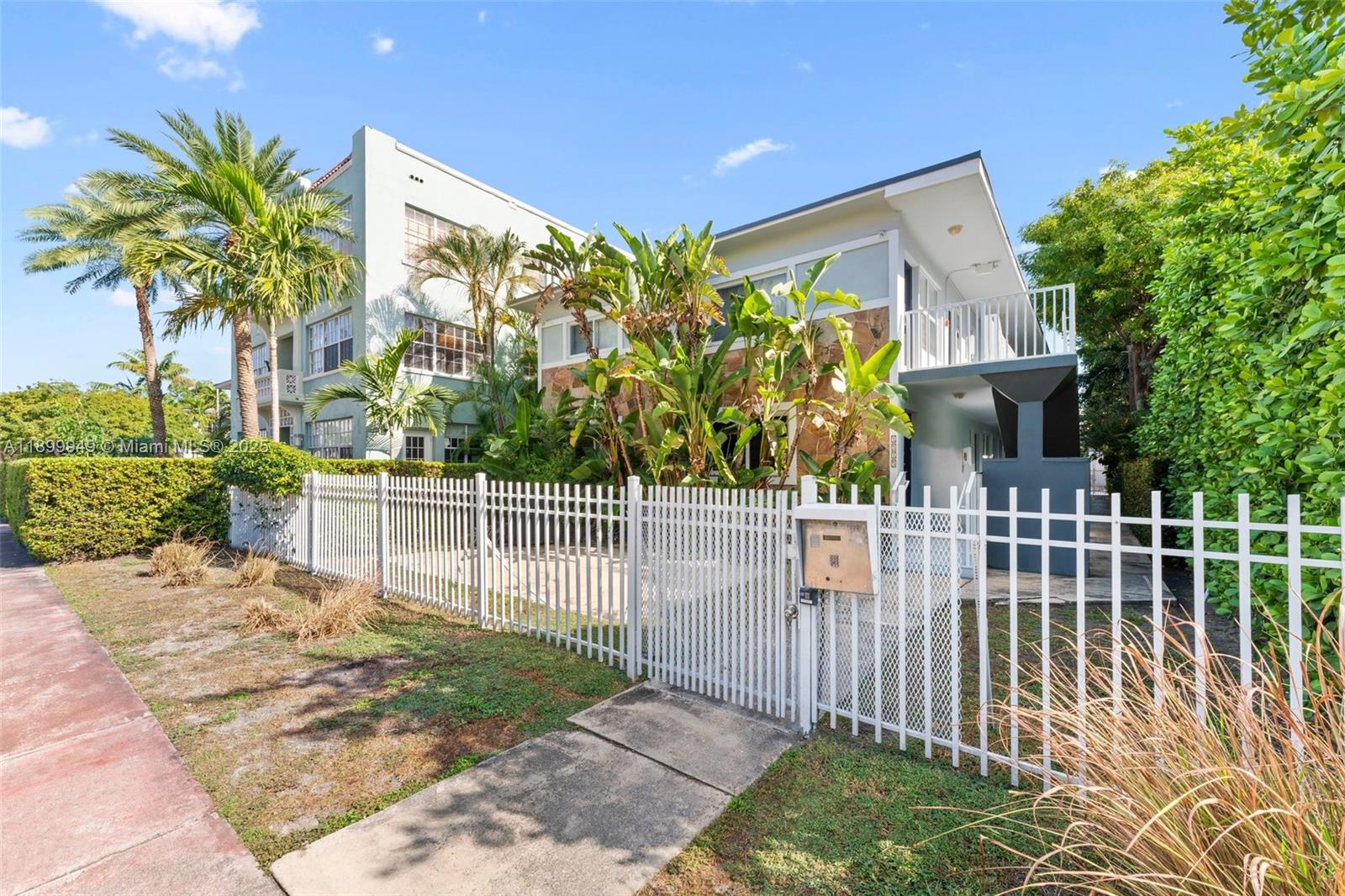 A white metal fence encloses the front yard of a two-story apartment building with landscaping — 1515 WEST AVE # 9, Miami Beach FL 33139, MIAMI BEACH, FL