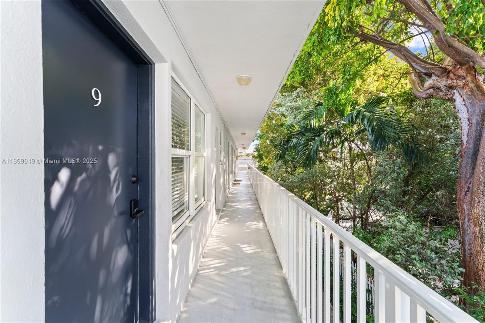 An outdoor apartment walkway features a dark door numbered nine and a white railing — 1515 WEST AVE # 9, Miami Beach FL 33139, MIAMI BEACH, FL