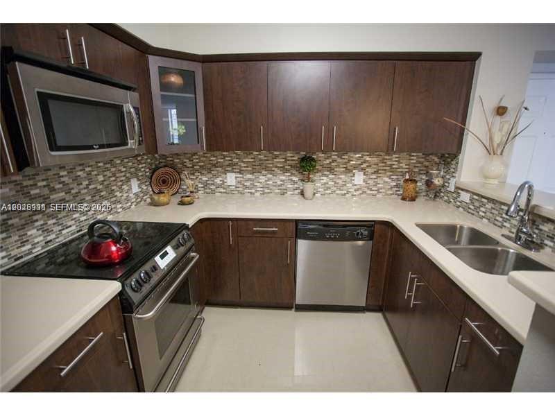 A kitchen features dark wood cabinets, stainless steel appliances, and a mosaic tile backsplash — DORAL, FL