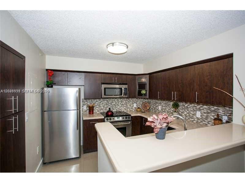 A kitchen features dark wood cabinets, stainless steel appliances, and a light-colored breakfast bar — DORAL, FL