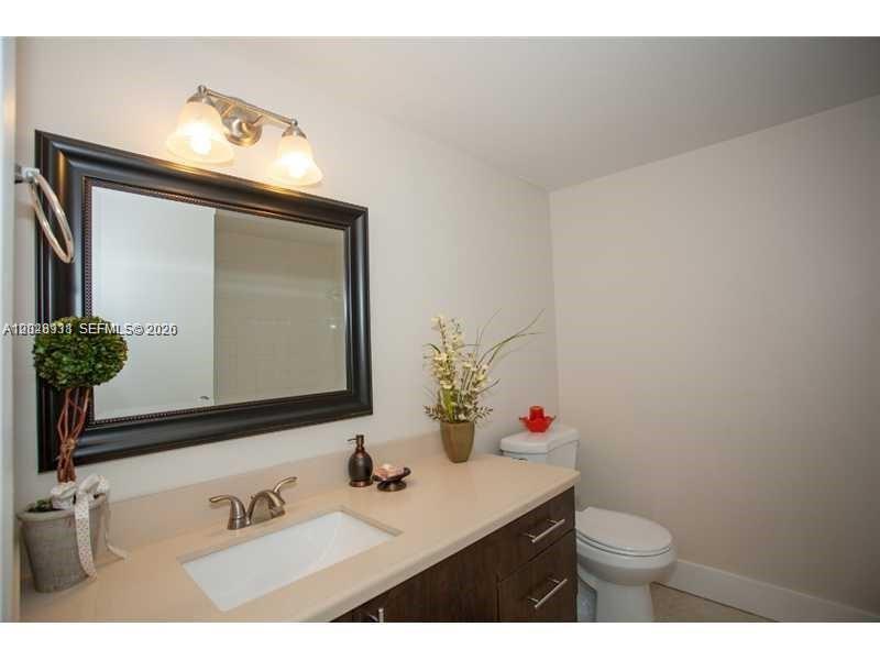 A bathroom features a dark-framed mirror, a light-colored vanity, and a white toilet — DORAL, FL