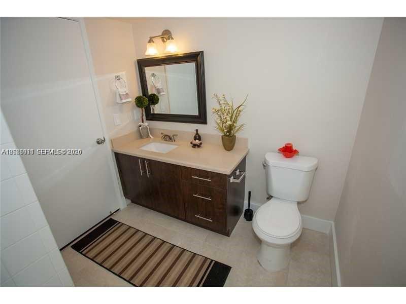 A bathroom features a dark wood vanity, a rectangular mirror, and a white toilet — DORAL, FL