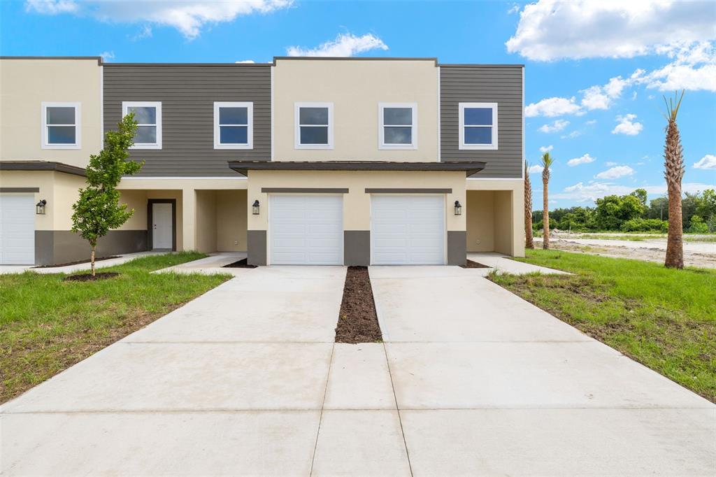A two-story townhouse exterior features a concrete driveway, two garage doors, and tan siding — 14985 SUNSET EVE LOOP, FORT MYERS, FL
