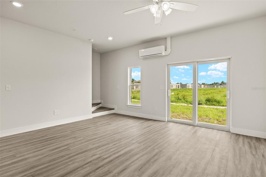 A bright living room features light wood-look flooring, a ceiling fan, and sliding glass doors — 14985 SUNSET EVE LOOP, FORT MYERS, FL