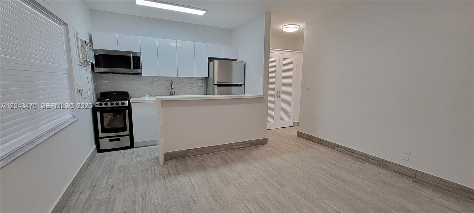 A kitchen with white cabinets and stainless steel appliances opens to a living area — 1723 Liberty St # 3, Hollywood FL 33020, HOLLYWOOD, FL