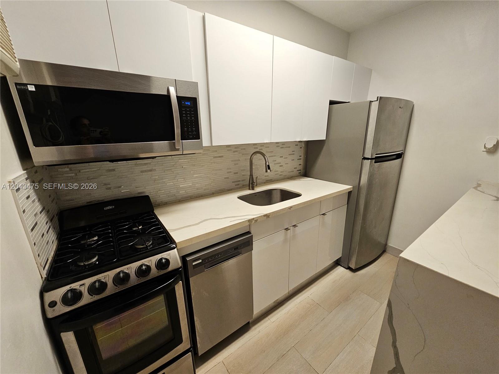A galley kitchen features white cabinets, stainless steel appliances, and a light-colored stone countertop — 1723 Liberty St # 3, Hollywood FL 33020, HOLLYWOOD, FL