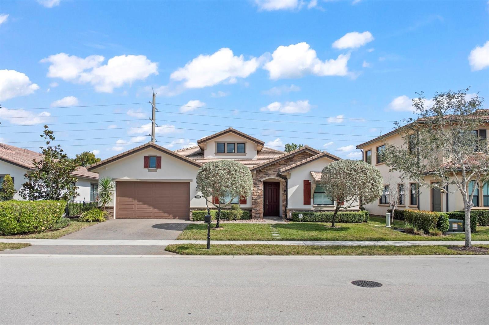 A single-story suburban house with a brown garage, stone accents, and a manicured front lawn — 8840 Watercrest Cir Circle E, Parkland FL 33076, PARKLAND, FL