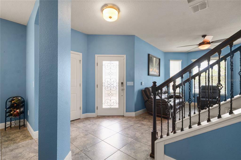 An entryway with light blue walls, tile flooring, a front door, and a wooden staircase — 5240 VILLA ROSA AVENUE, ST CLOUD, FL