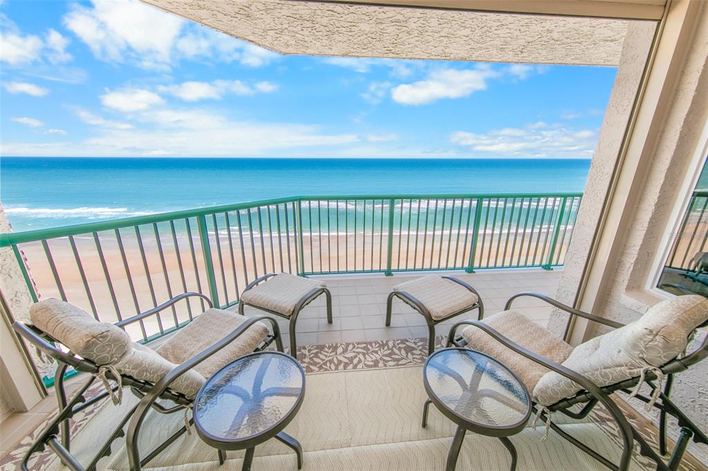 A balcony with two chairs, ottomans, and small tables overlooking the ocean and beach — 3315 S ATLANTIC AVENUE UNIT 1005, DAYTONA BEACH, FL