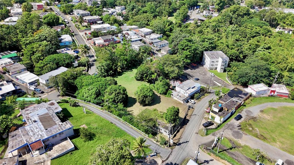 An aerial view shows a residential neighborhood with houses, green spaces, and paved roads — PR-876 KM 0.7 BO LAS CUEVAS, TRUJILLO ALTO, PR