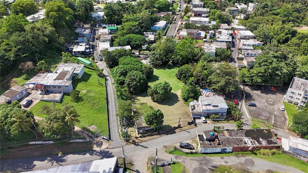 An aerial view shows a residential neighborhood with houses, green spaces, and intersecting paved roads — PR-876 KM 0.7 BO LAS CUEVAS, TRUJILLO ALTO, PR