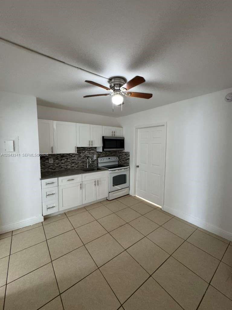 A kitchen features white cabinets, a tiled backsplash, stainless steel appliances, and beige floor tiles — NORTH MIAMI, FL
